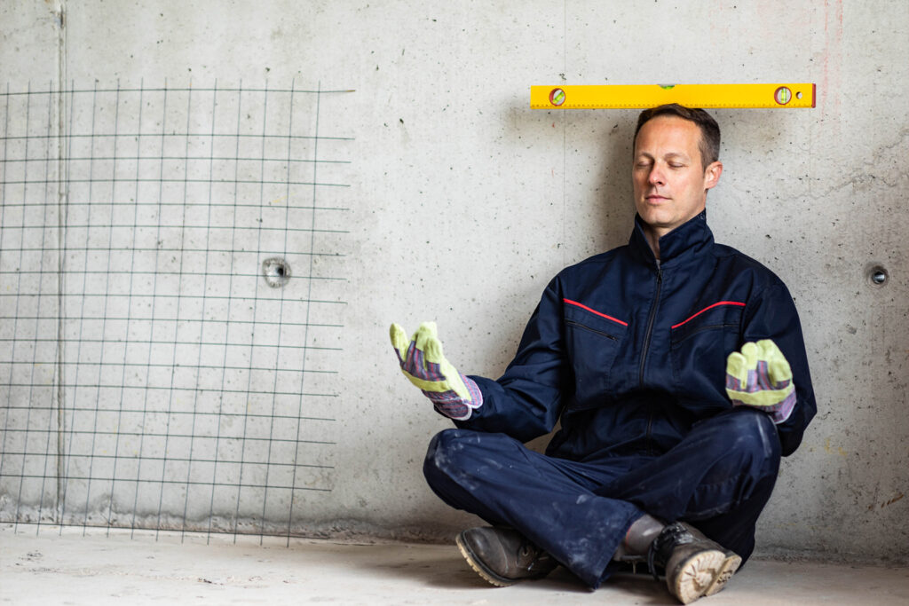 Arbeiter sitzt auf dem Boden balanciert Wasserwaage auf dem Kopf